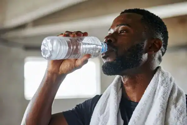 Image of man drinking water to improve hydration Godalming after work out.